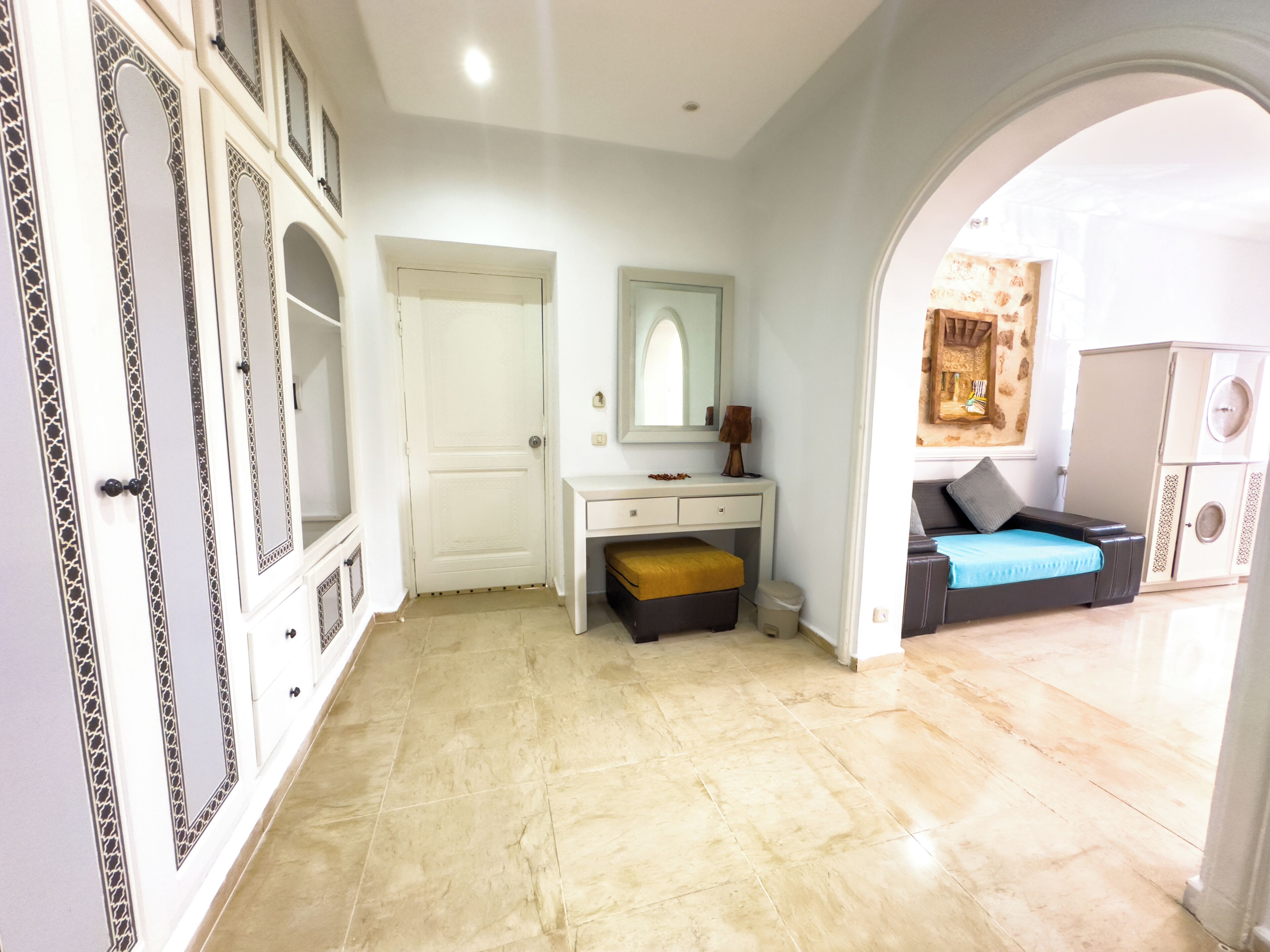 A room with a white vanity, a mirror, a small bench, and a bed with a blue bedspread.