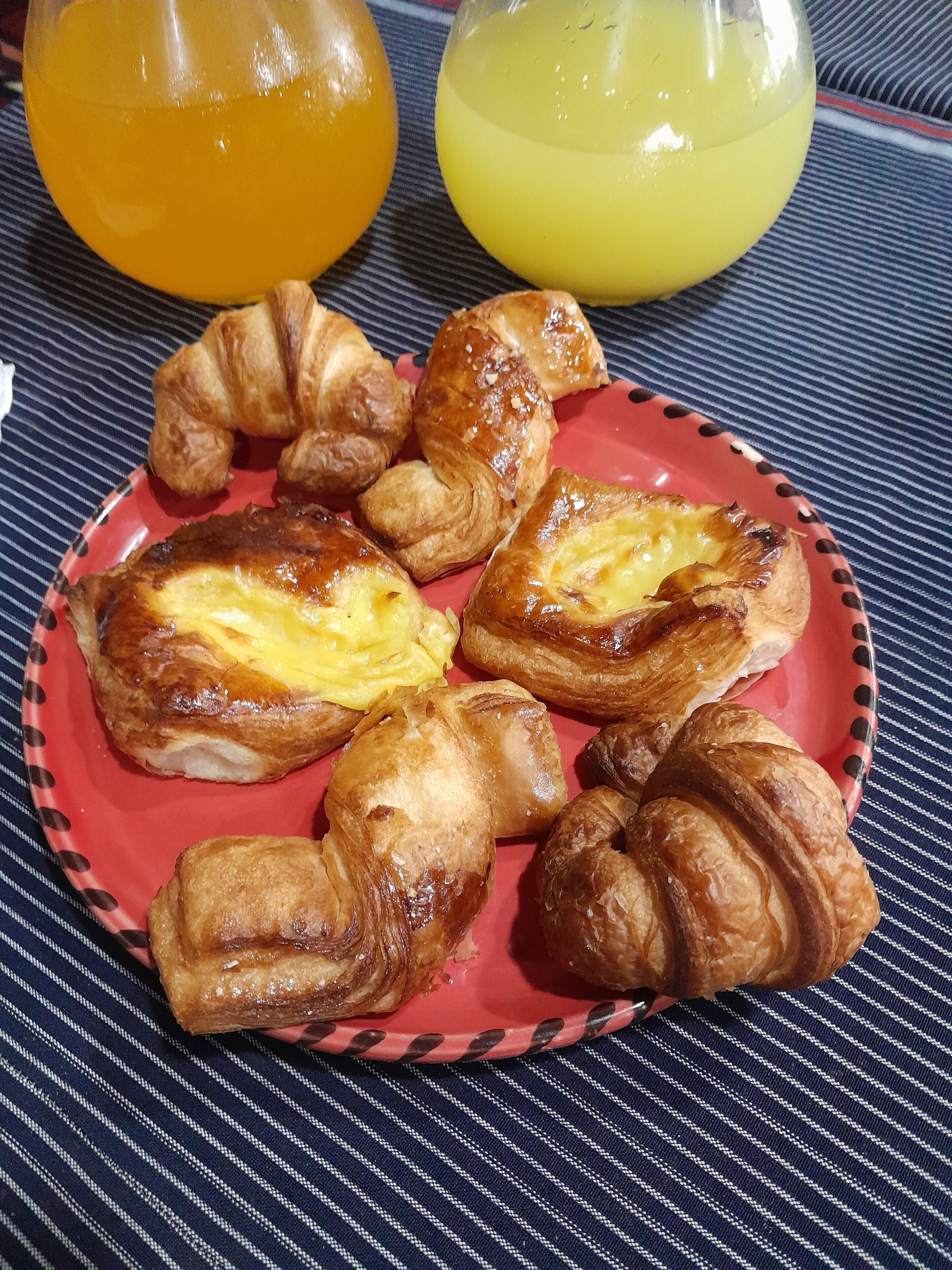 A plate of croissants and a glass of orange juice on a striped tablecloth.