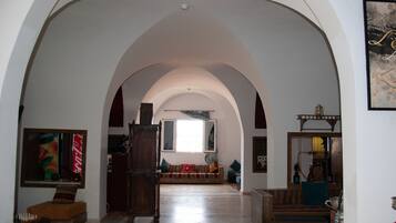 Un vaste hall d’entrée avec de hauts plafonds en arc de cercle, un meuble en bois, un canapé avec des coussins et un narguilé sur la droite.