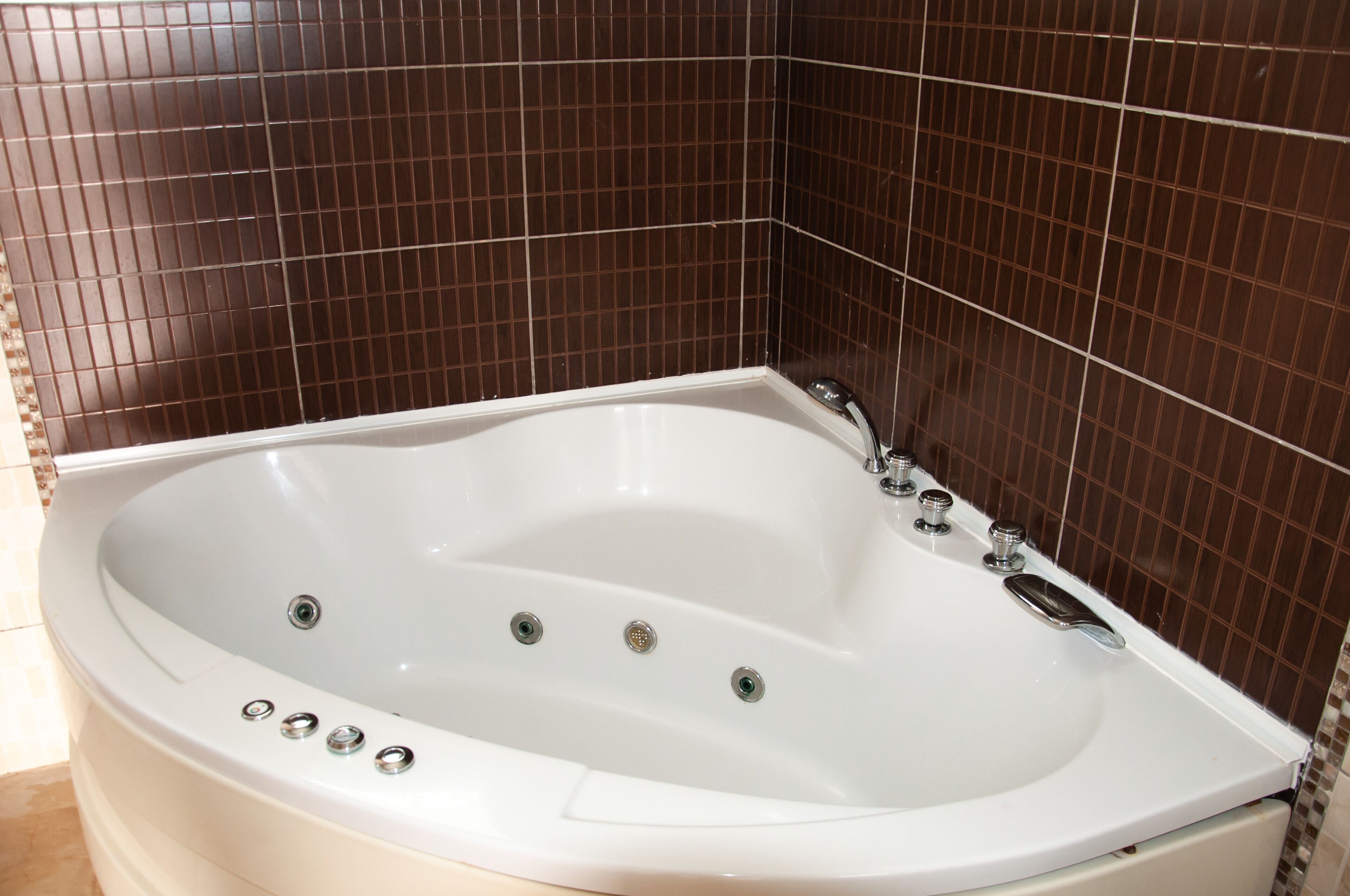 Une baignoire blanche dotée de plusieurs jets, dans une salle de bain dont les murs sont recouverts de carreaux marron.