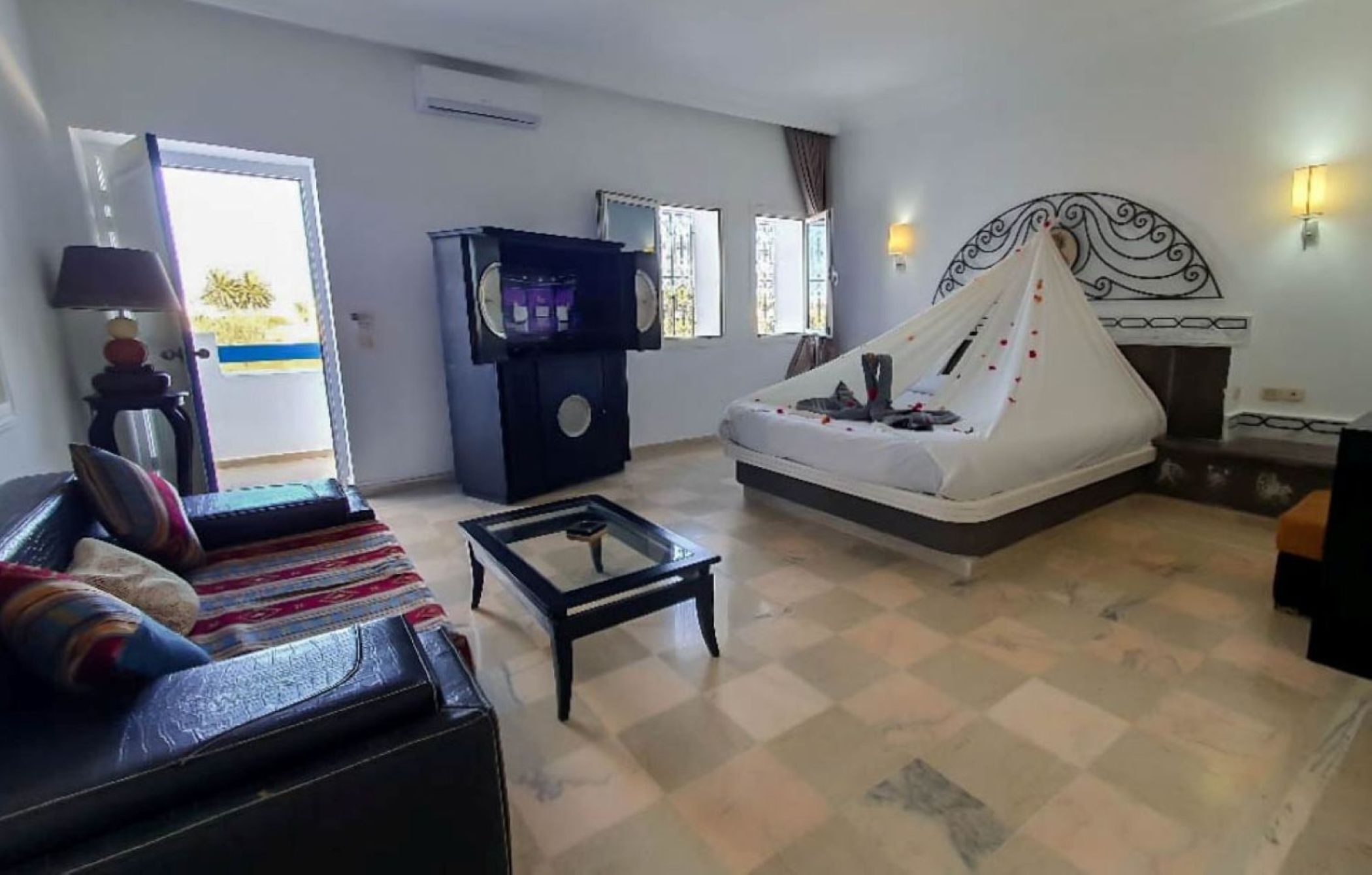Quarto de hotel com sofá, mesa de centro, cama com dossel, televisão e lareira.