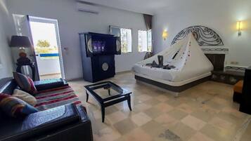 Quarto de hotel com sofá, mesa de centro, cama com dossel, televisão e lareira.