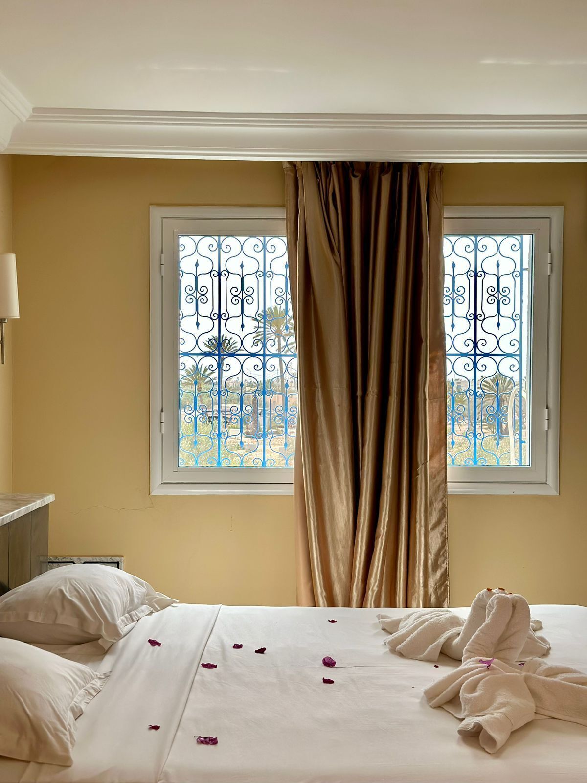 A hotel room with a bed, two windows with metal grilles, a curtain, and a bedside lamp.