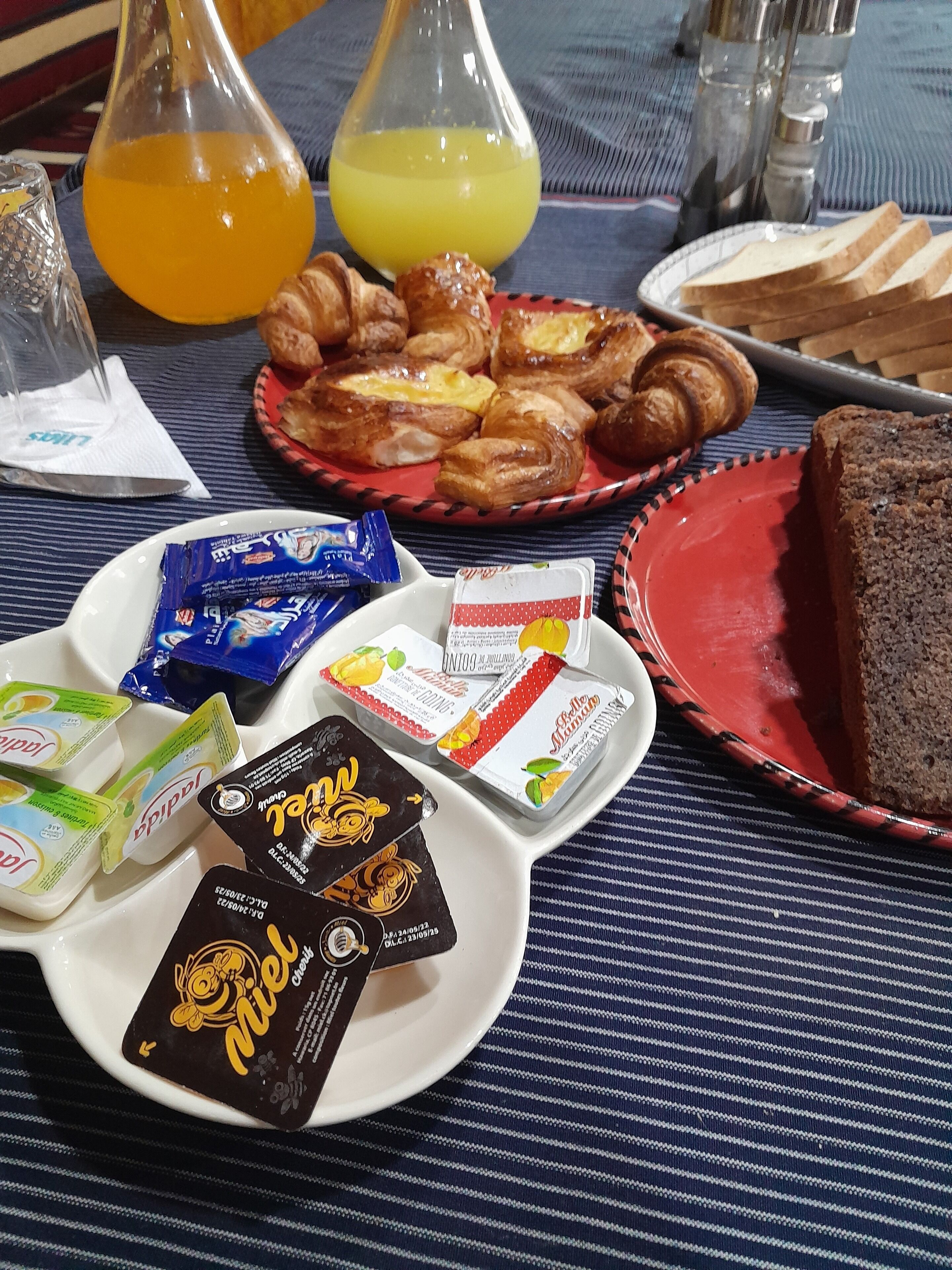 A breakfast table with croissants, bread, juice, and packaged food items.