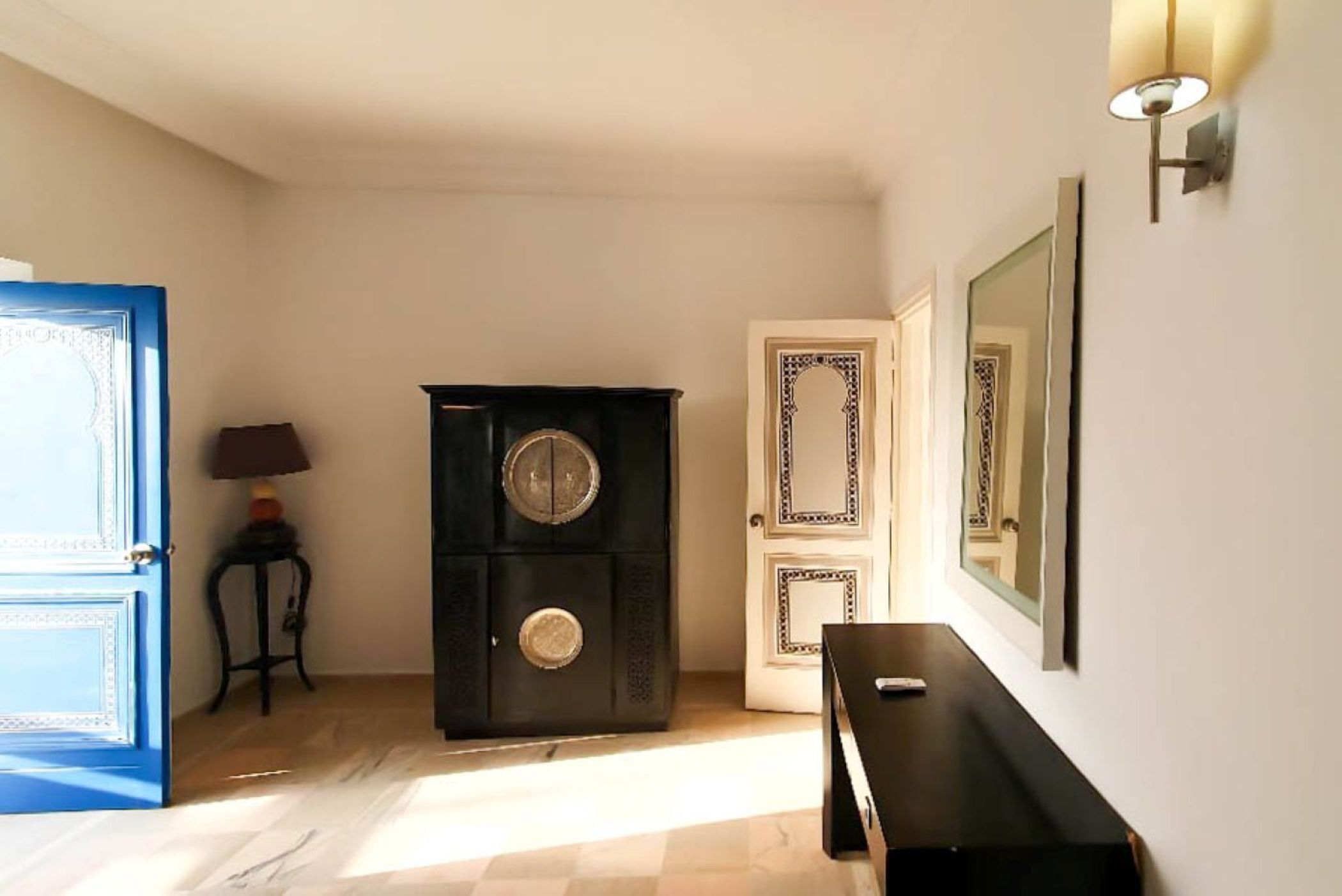 Un pasillo con una puerta azul, un armario negro, una puerta blanca con paneles decorativos y un espejo montado en la pared.