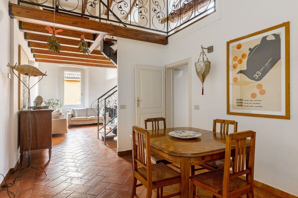 A dining area with a wooden table and chairs, a staircase with wrought iron railings, and a view of a living room with a sofa and a window. - Country Style House in Bologna by Wonderful Italy (Bologna)