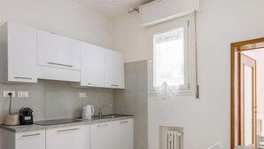 Een moderne keuken met witte kasten, een aanrecht, een waterkoker en een raam met zonwering.