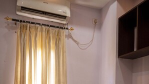 Et hotelværelse med seng, stol, aircondition, et vindue med gardiner og en vægmonteret hylde.
