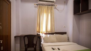 Et hotelværelse med seng, skrivebord, stol, aircondition og et vindue med gardiner.