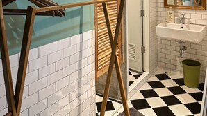 Un baño con piso a cuadros, un tendedero de madera, un lavamanos y un espejo.