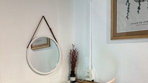 Un escritorio blanco con un espejo, un florero con flores secas y una obra enmarcada en la pared.