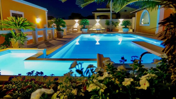 Una piscina con zona a livello ribassato, circondata da piante in vaso e mobili da esterno.