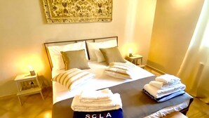 Un letto rifatto con cuscini e una coperta piegata, un comodino con una lampada e un'opera d'arte appesa al muro.