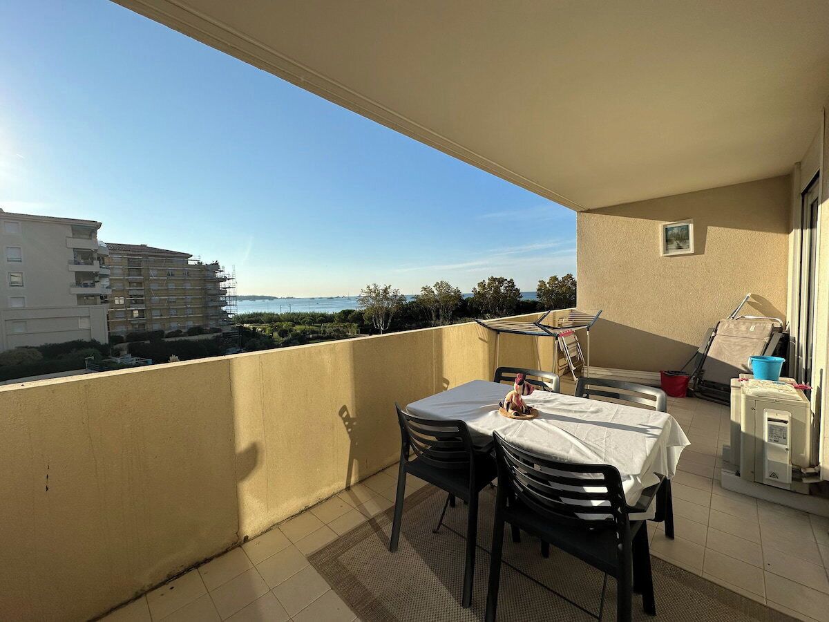 A balcony with a table and chairs, a small table with a basket, and a window.