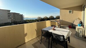 Un balcón con mesa y sillas, una mesita con una cesta y una ventana.