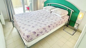 Una cama individual con una colcha estampada con motivos florales, cabecera verde y una mesita de noche con lámpara.