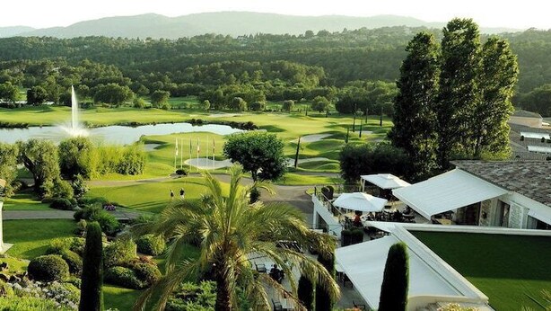 Un campo de golf con un estanque, palmeras y un edificio de techo blanco.