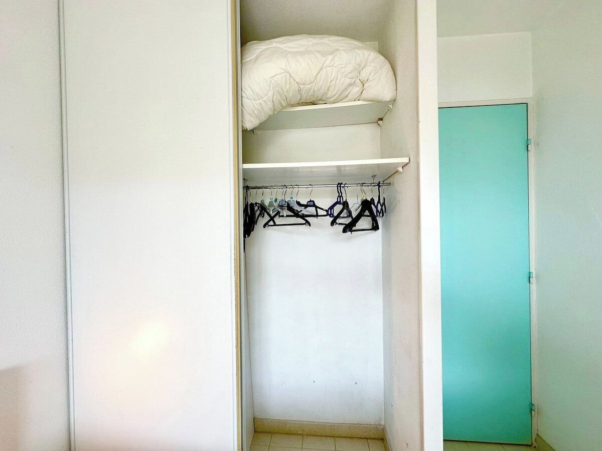Un armario con una cama en la parte superior, una percha y una puerta color turquesa.