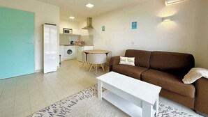 Un espacio habitable compacto con kitchenette, un sofá marrón, una mesa de centro blanca y una alfombra estampada.
