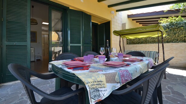 Un espace de restauration en plein air avec une table dressée pour quatre personnes, protégée par un parasol vert et entourée d’un sol en pierre.