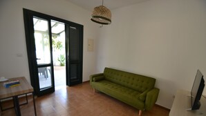 Une pièce avec un canapé vert, une table en bois, un téléviseur et une porte donnant sur l’extérieur.