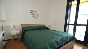 Une chambre avec un lit en bois, une couvre-lit verte, une décoration murale représentant des poissons, une petite table de chevet avec une lampe et une fenêtre donnant sur l’extérieur.