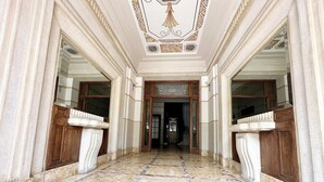Un vaste hall d’entrée doté d’un sol en marbre, d’un plafond richement décoré et de portes en bois.