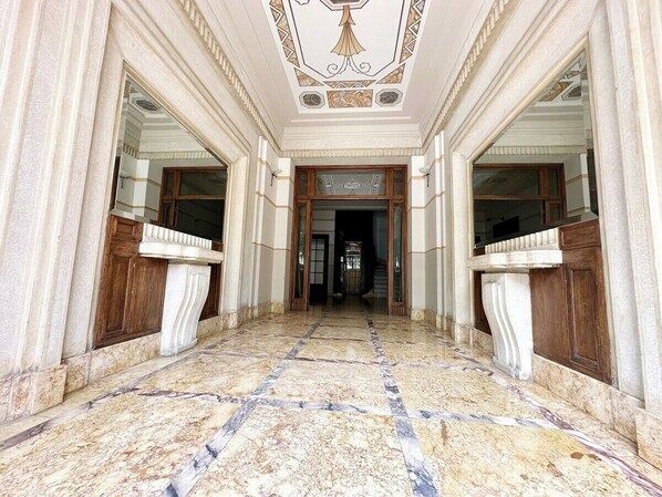 A grand hallway with marble flooring, ornate ceiling, and wooden doors.