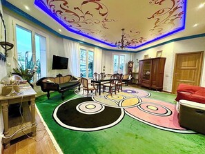 A living room with a green carpet, a TV, a piano, and a dining area with chairs.