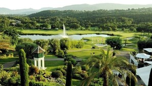 Un parcours de golf avec un étang, des palmiers et une chaîne de montagnes en arrière-plan.