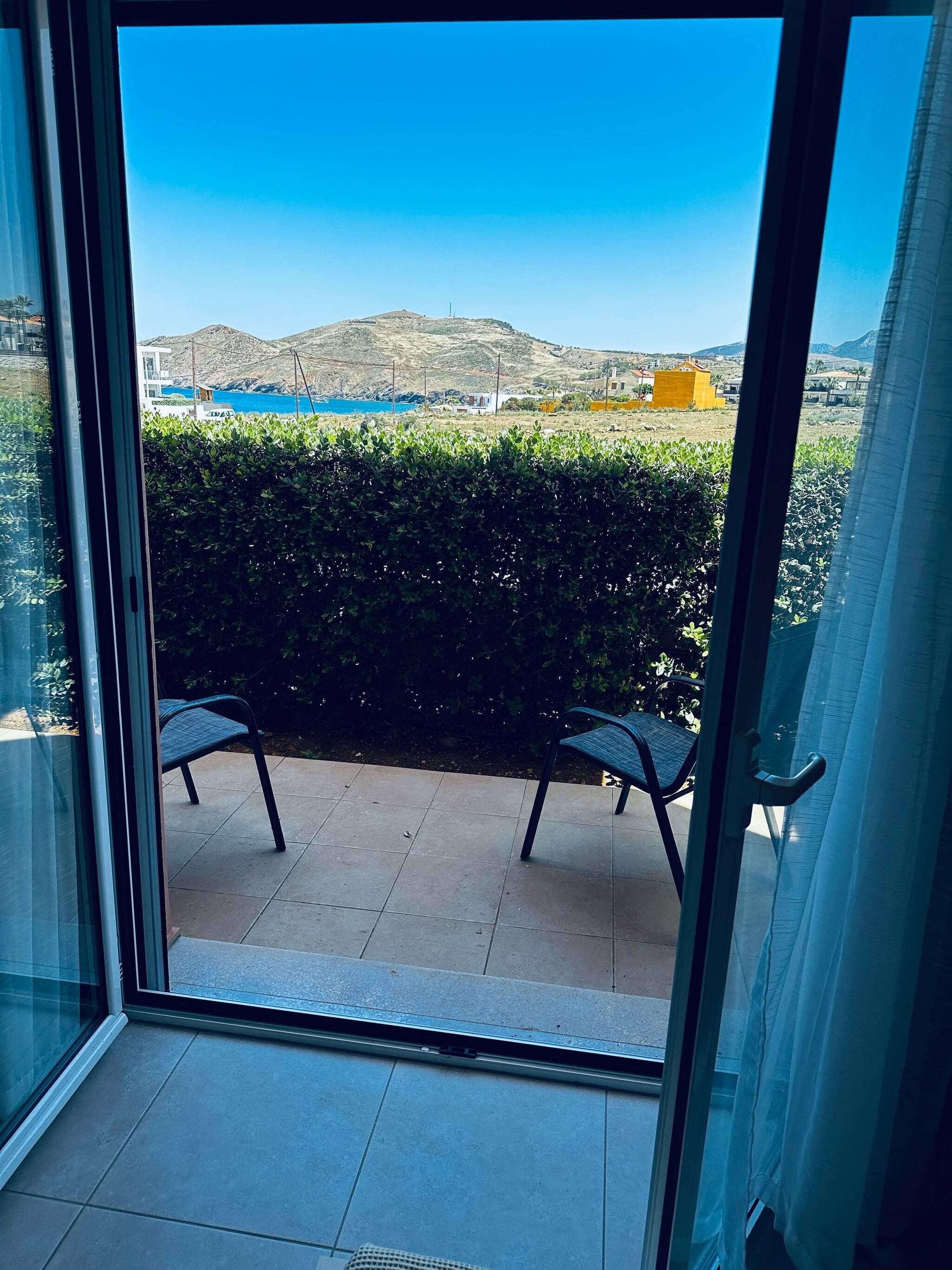 Un balcon avec deux chaises, une vue sur une mer bleue et une montagne en arrière-plan.