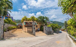 Traditional house surrounded by lush greenery and a scenic hilly backdrop.