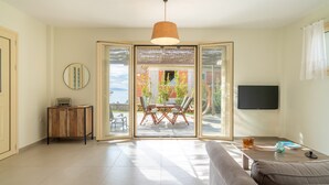 A living room with a sofa, a coffee table, a TV, and a sliding glass door leading to an outdoor patio. - The Cerulean Villa - The Concord Of Blue And Green! (Kefalonia)