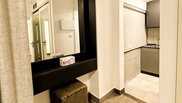 A bathroom with a large mirror, a towel rack, a toilet, and a shower area. - Central Apartment For Rent 31 (Amman)