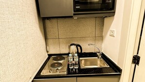 A compact kitchen with a microwave, stove, and sink. - Central Apartment For Rent 31 (Amman)