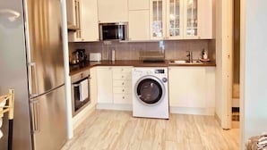 A compact kitchen with a refrigerator, microwave, oven, washing machine, and a sink. - Charming Studio Flat In Sollentuna, Stockholm (Sollentuna)