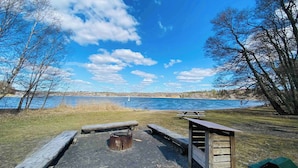 A lakeside picnic area with benches, a fire pit, and a wooden shelter. - Charming Studio Flat In Sollentuna, Stockholm (Sollentuna)