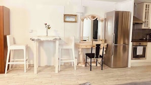 A compact living space with a kitchenette, a dining area with two chairs, a small table with a vase, a mirror, and a refrigerator. - Charming Studio Flat In Sollentuna, Stockholm (Sollentuna)