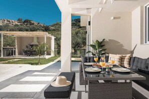 Un espace extérieur moderne aménagé pour les repas, avec une table dressée pour le petit-déjeuner, un canapé et une pergola dotée d’un barbecue.