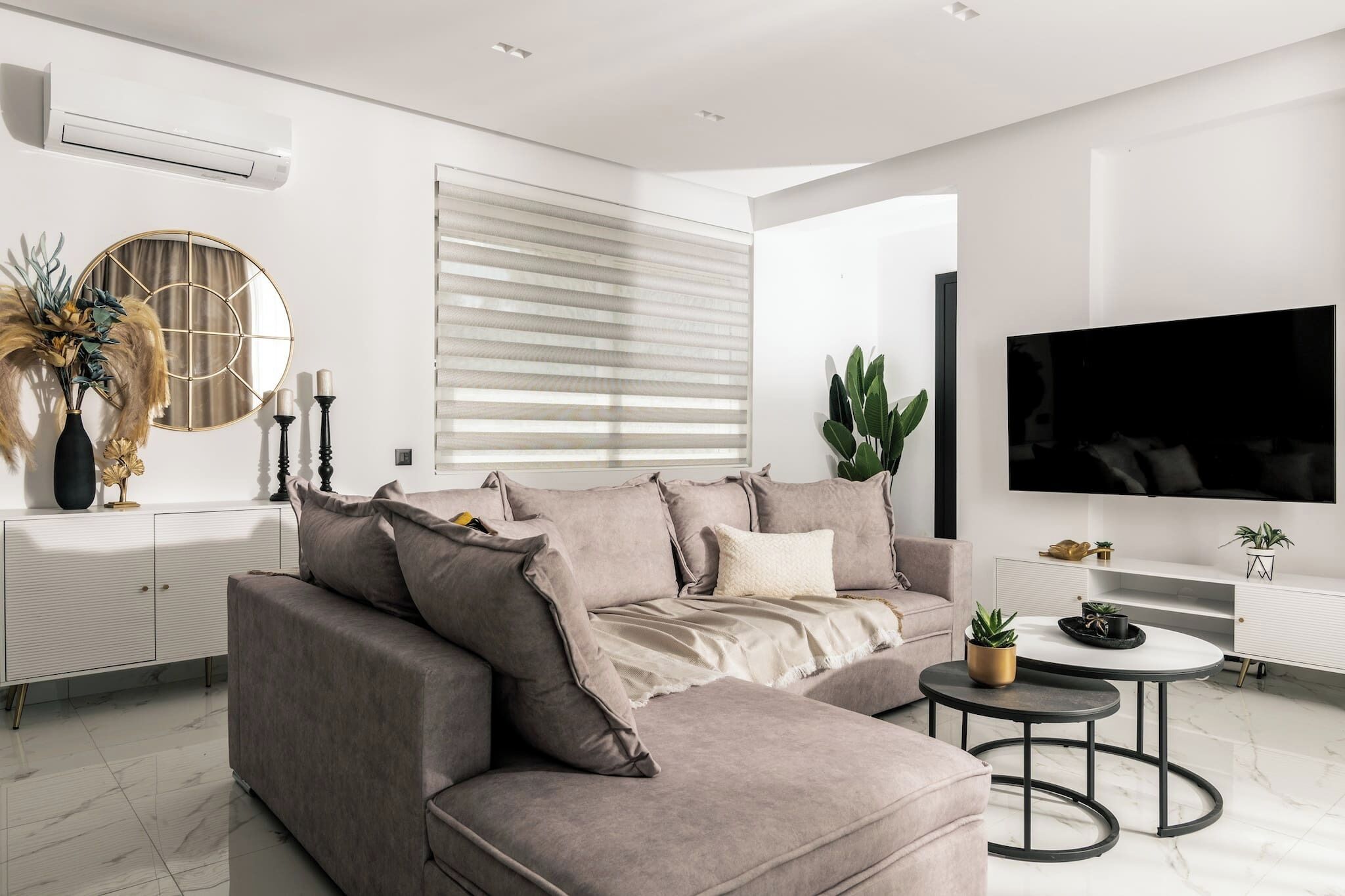 A modern living room with a sectional sofa, a flat-screen TV, a round coffee table, and a white console.