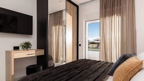 A modern bedroom with a bed, a desk, a TV, and a view of the outdoors. - Melissia Luxury Villa (Zakynthos)