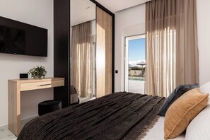 Ein modernes Schlafzimmer mit Bett, Schreibtisch, Fernseher und Blick ins Grüne.
