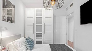 Une chambre à coucher avec un lit, une armoire blanche et un téléviseur fixé au mur.