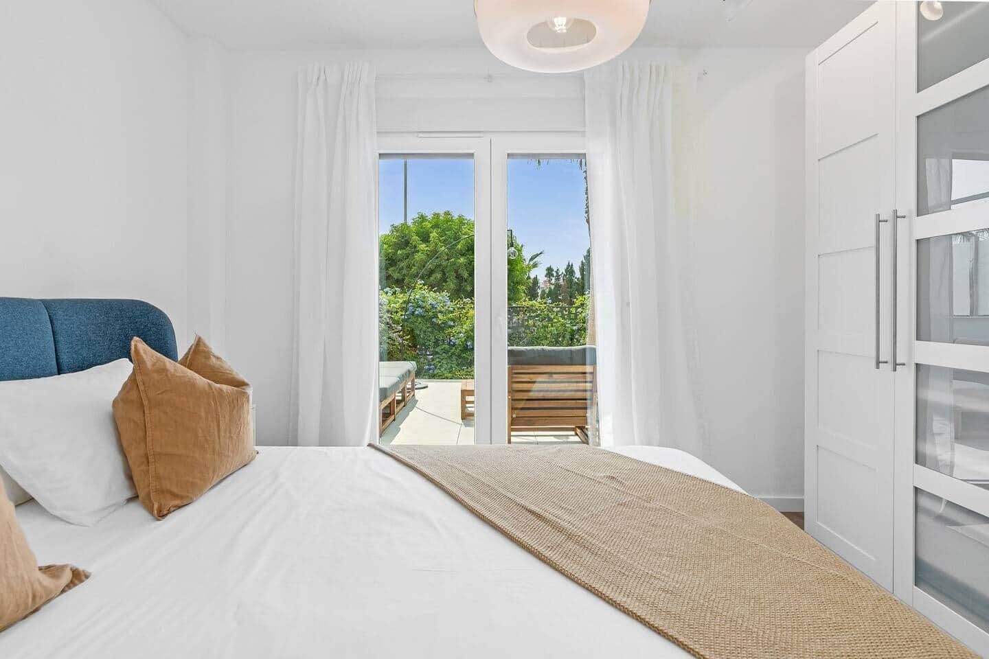 Ein Schlafzimmer mit Bett, Kissen, einem Nachttisch und Blick auf einen Balkon.