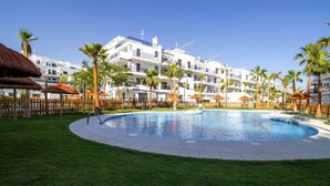 Une piscine entourée de palmiers et un bâtiment blanc doté de balcons.