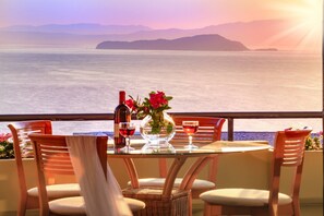 A table with chairs, a bottle of wine, and a vase with flowers, overlooking a body of water with distant land. - Koralia - Chania's Card Postal Villa Majestic View (Chania)
