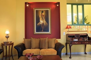 A room with a sofa, a desk, a lamp, and a framed painting on the wall.