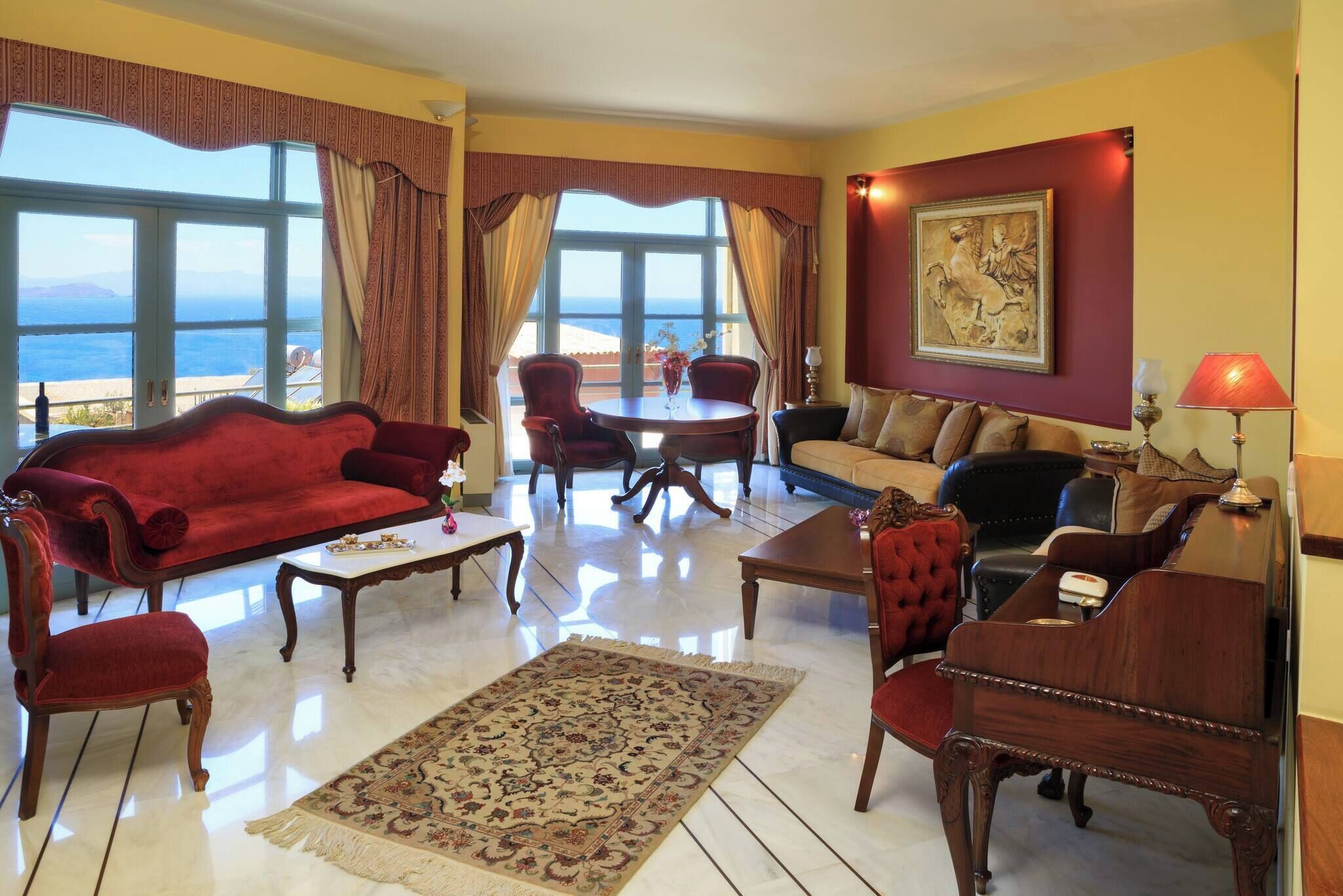 Una habitación con un sofá rojo, una mesa de centro de madera, un tapiz estampado, un sofá beige y un cuadro en la pared.