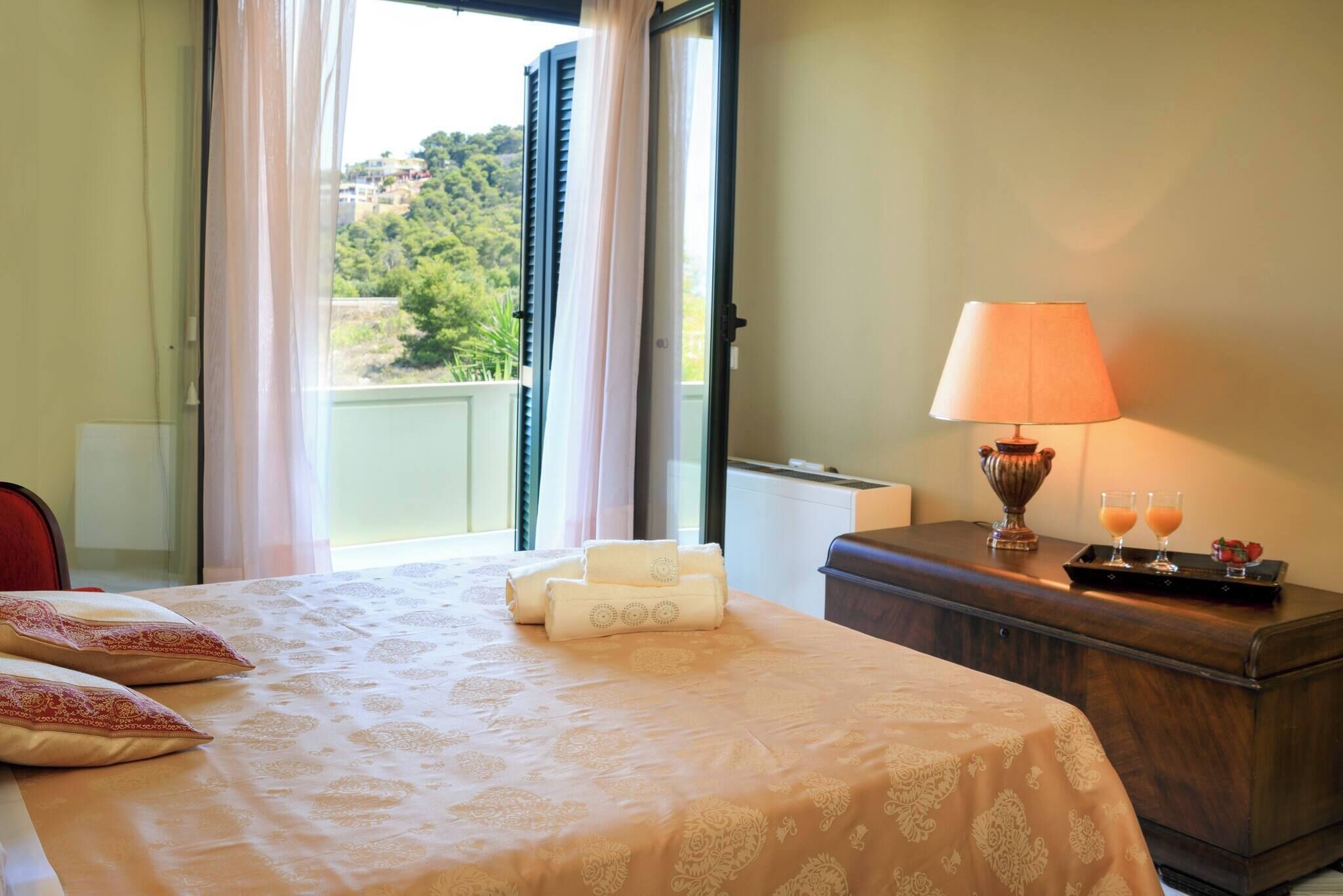 Quarto de hotel com cama, mesa de cabeceira e luminária, e vista para o verde lá fora.