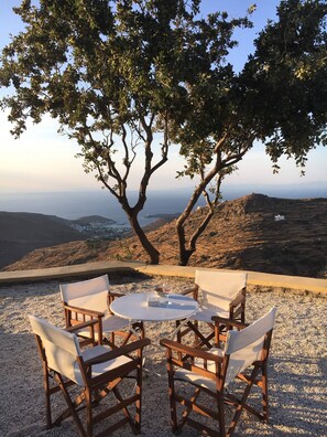 A table with four chairs under a tree, overlooking a coastal landscape.